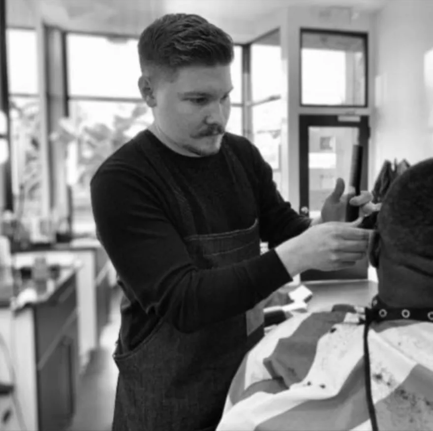 A barber trimming a client's hair near a shop window