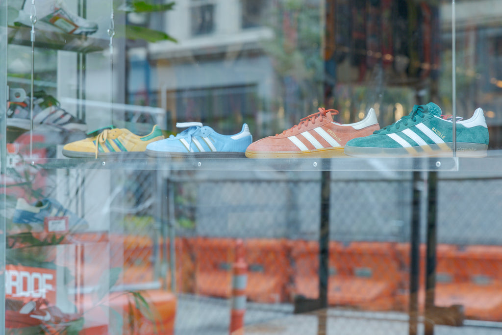 Colorful Adidas sneakers displayed in the store's front window, with the Downtown Cincinnati street reflected in the glass.